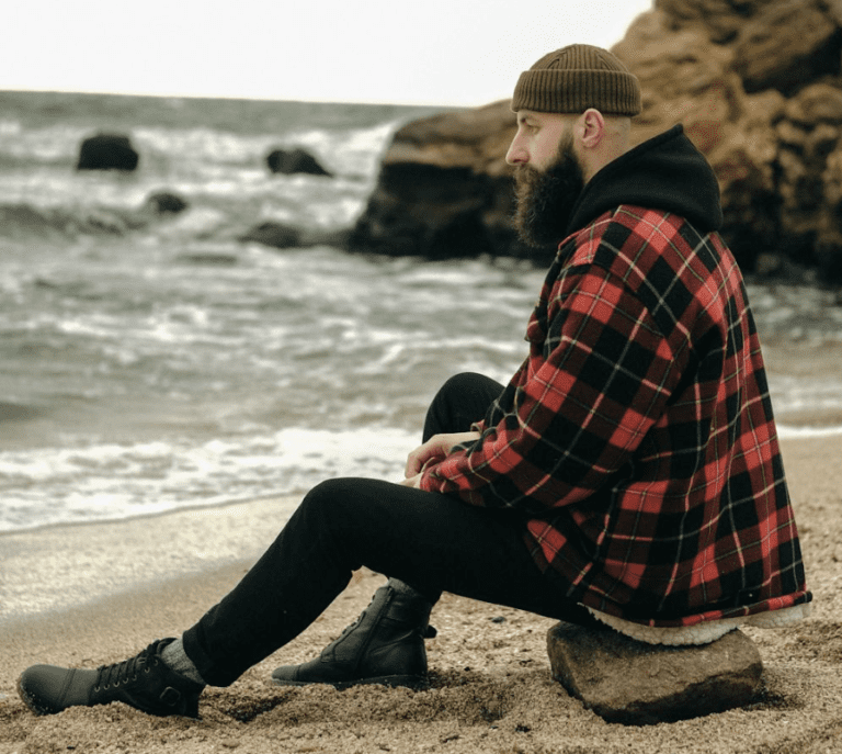 men's fall casual outfits featured image man wearing flannel and jeans and boots by the beach